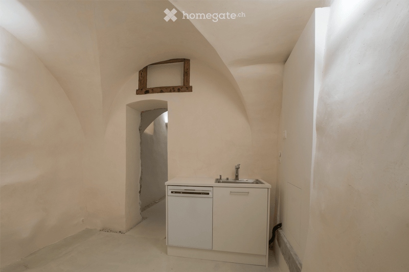 Minimalist kitchen with white cabinetry, sink, and dishwasher, set in a room with arched ceilings and natural light.