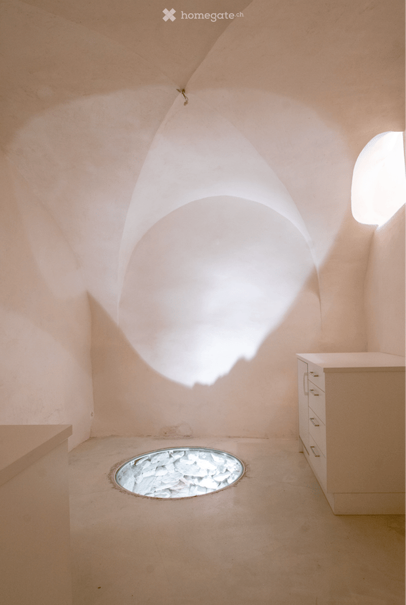 Minimalist unfurnished room with light-colored walls and floor, featuring a unique circular skylight and a small round opening in the floor.