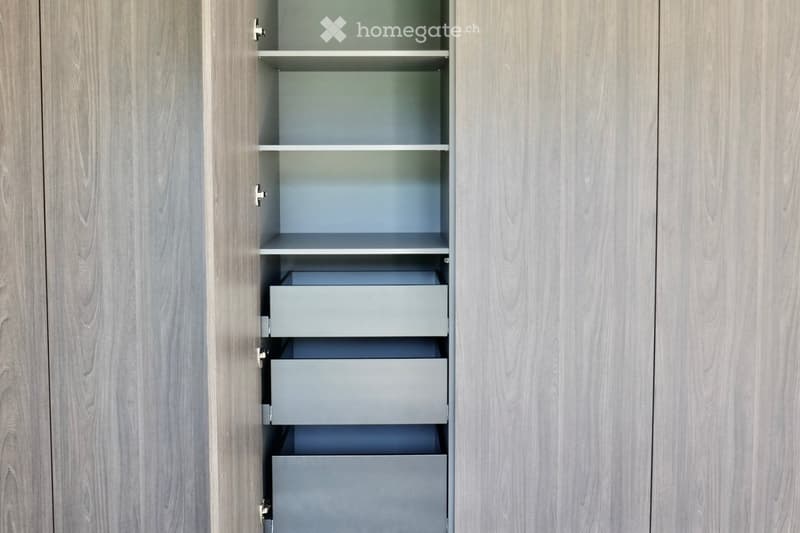 An empty, modern wardrobe with light wood panels and multiple empty shelves and drawers.