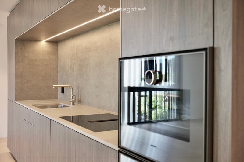 Modern kitchen with light wood cabinets, a double sink, and a sleek faucet. The space features built-in lighting and a large window offering a view of the outdoors.