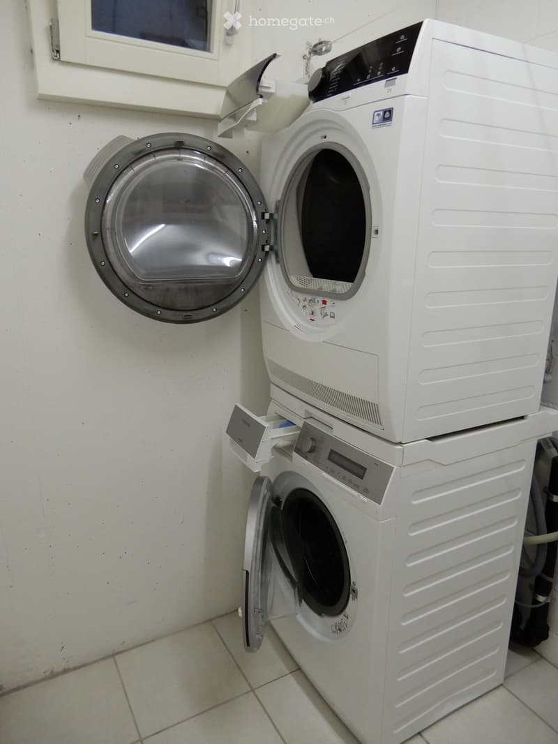 A compact bathroom with a stacked washing machine and dryer unit, both white, with open doors showing the interior.