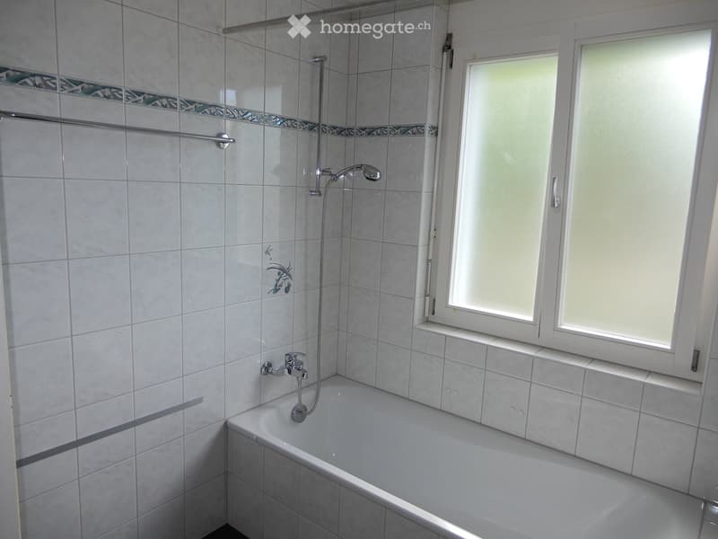 Modern bathroom with a bathtub, tiled walls, a showerhead, and a window with frosted glass.