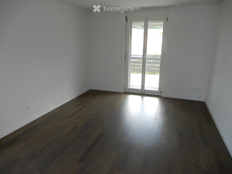 Empty room with wooden flooring and white walls, featuring a large sliding glass door leading outside.