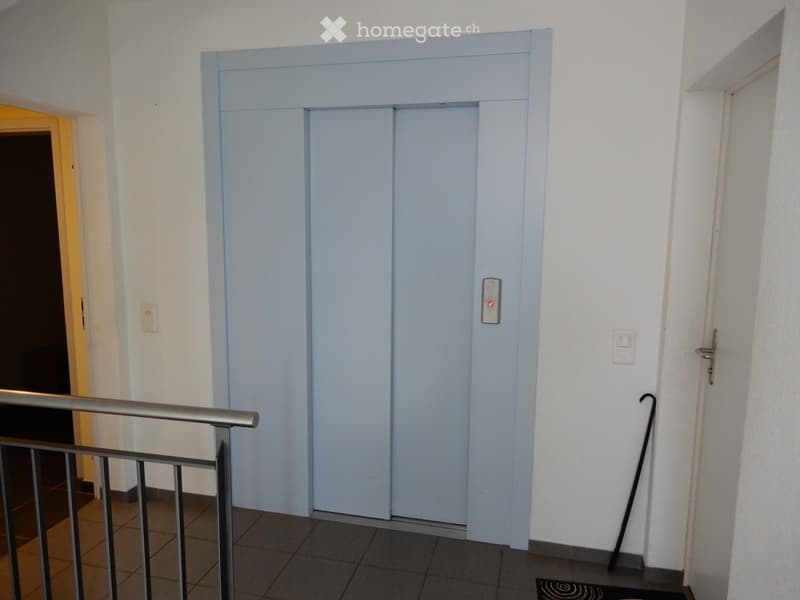 Hallway with elevator doors, metal railing, and tiled floor.