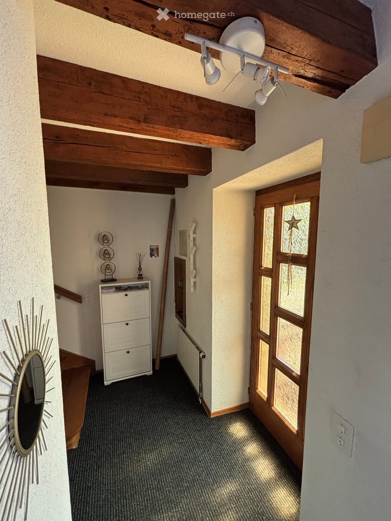 Carpeted hallway with wooden beams on the ceiling, a small cabinet with drawers, a mirror on the wall, and a door leading to another room.