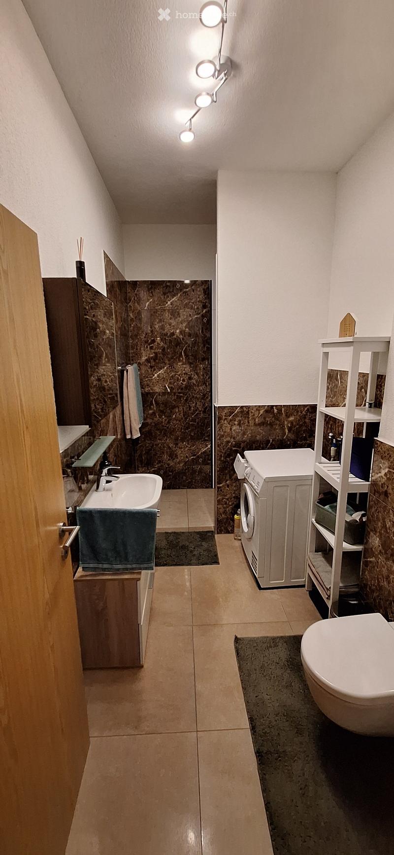 Bathroom with beige tiled floor, marble accent wall, sink with faucet, toilet, washing machine, and storage cabinet.