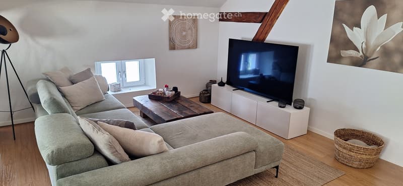 Modern living room with a grey sectional sofa, wooden coffee table, flat-screen TV on a white stand, floor lamp, and decorative artwork on the walls.