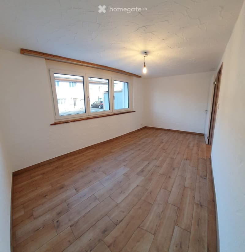 Empty room with wooden flooring, white walls, and a large window with wooden trim. The room has a simple, clean design with no furniture or decorations.