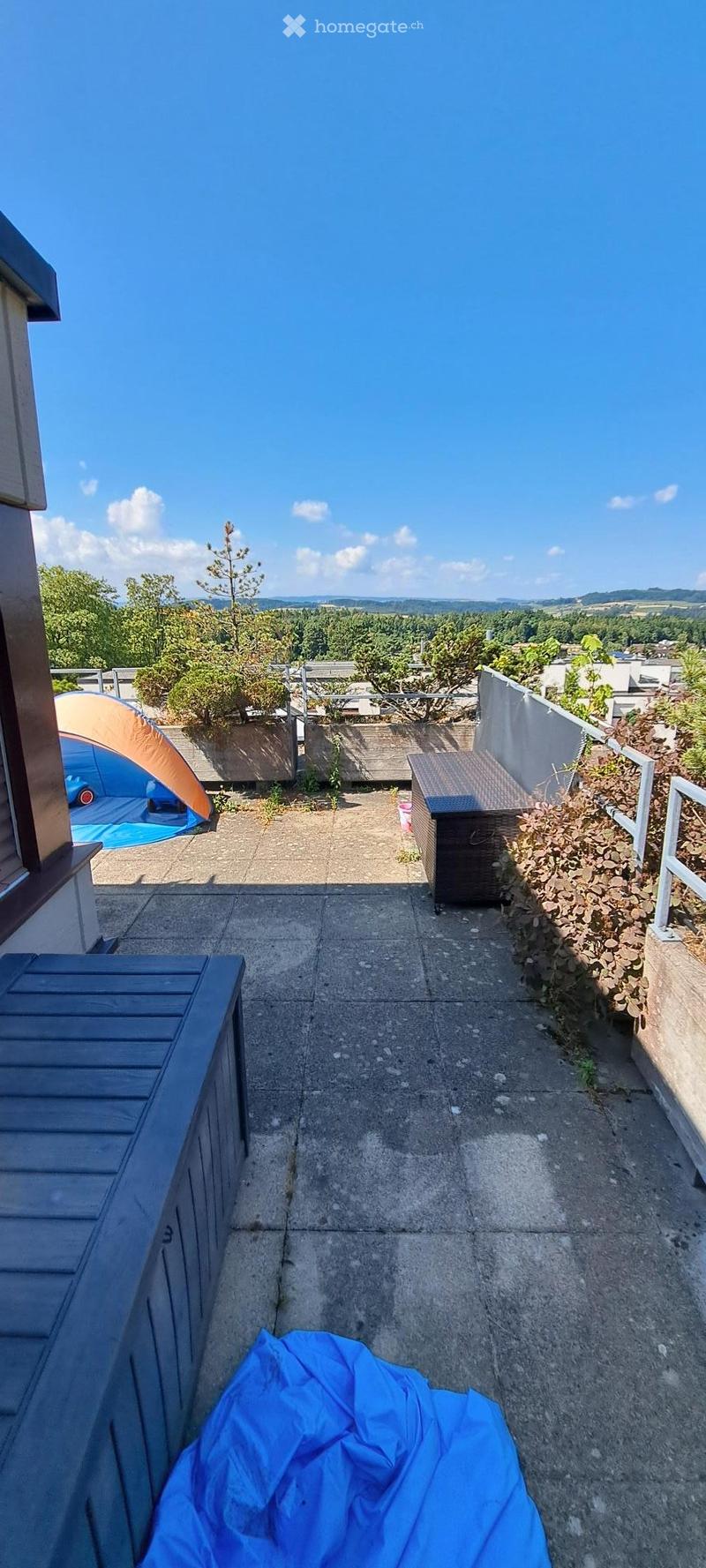 Concrete balcony with wooden benches, small tent, and scenic view of greenery and hills.