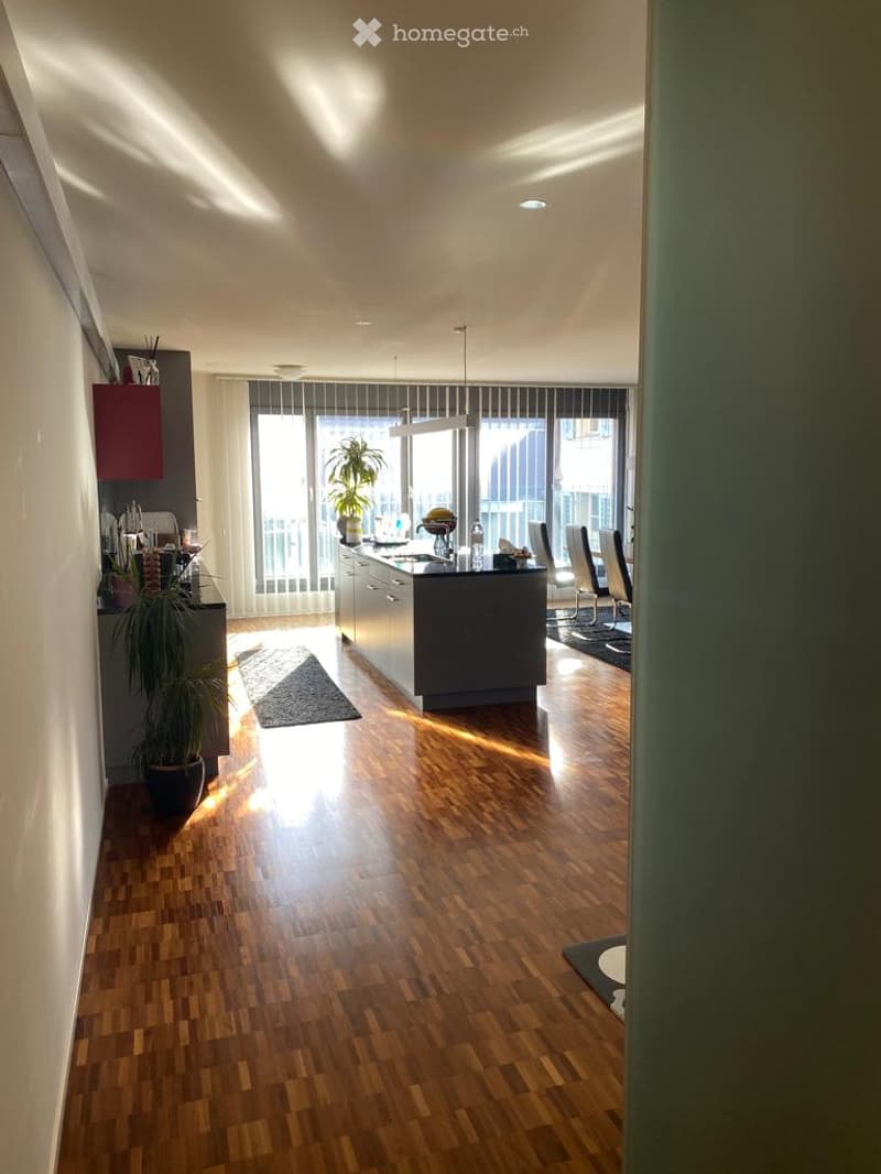 Open-plan kitchen and dining area with wooden flooring, modern kitchen island, pendant lighting, and large windows leading to a balcony.