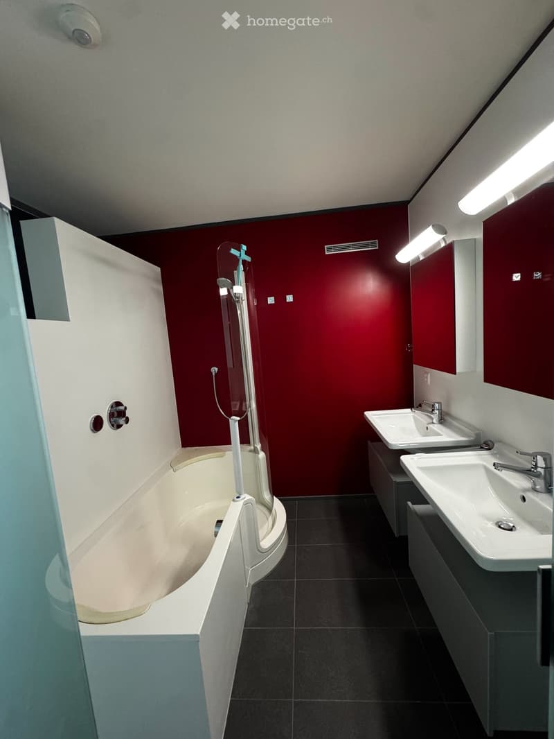 Modern bathroom with a white bathtub, two sinks, and red accent wall.