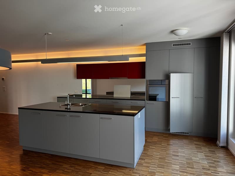 Modern kitchen with grey cabinets, a central island, stainless steel appliances, and wooden flooring.