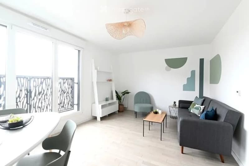 Modern living room with large windows and balcony access, featuring a grey sofa, coffee table, armchair, white shelving unit, and decorative wall art.