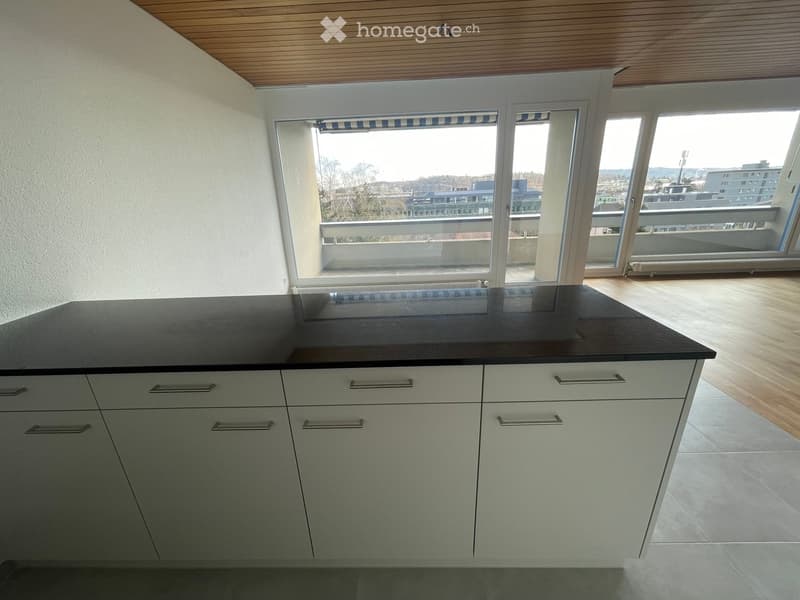 Modern kitchen with white cabinets, black countertop, and large windows offering a view of the city.
