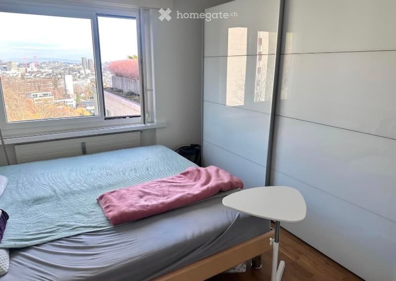 Modern bedroom with a double bed, nightstand, and large wardrobe. The room features large windows offering a city view.