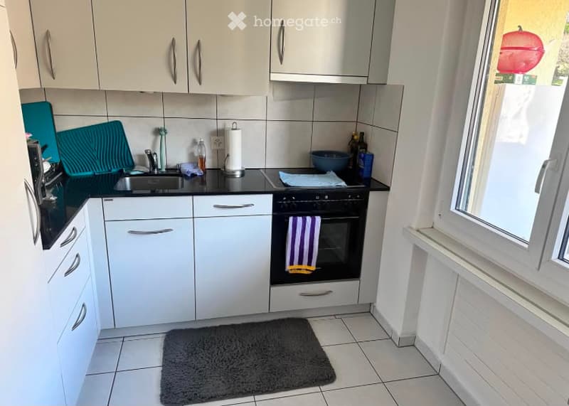 Modern kitchen with white cabinets, black countertops, and stainless steel appliances. Features a sink, oven, and various kitchen items on the counter.