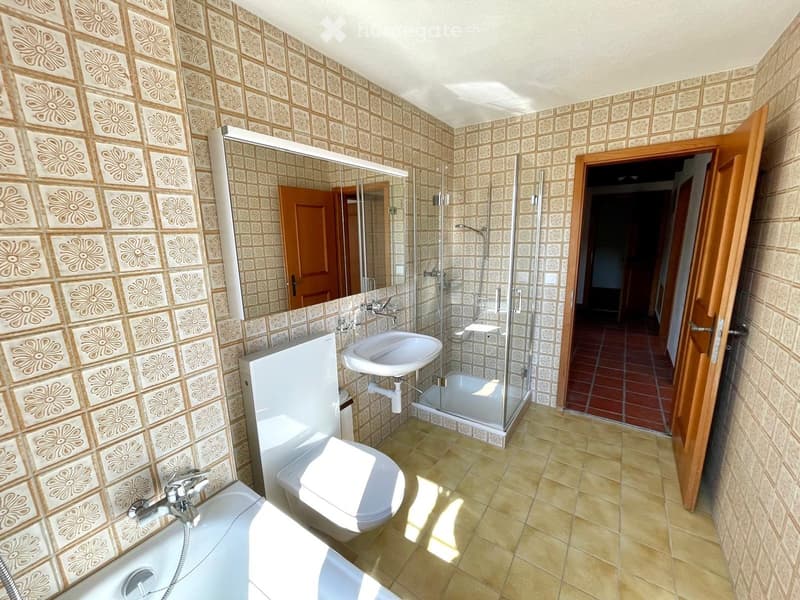 Bathroom with floral patterned tiles, bathtub, toilet, sink, and a glass-enclosed shower. A large mirror is mounted on the wall above the sink.
