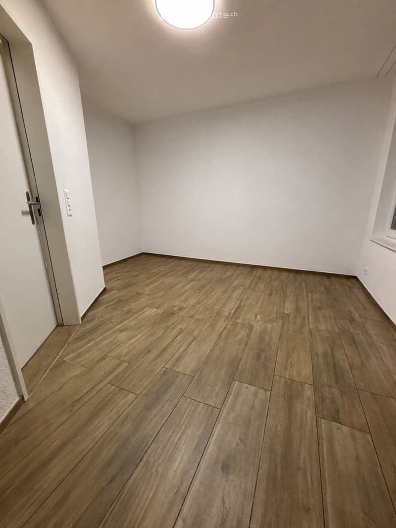Empty room with wooden flooring, white walls, and a round ceiling light fixture. No furniture or equipment present.