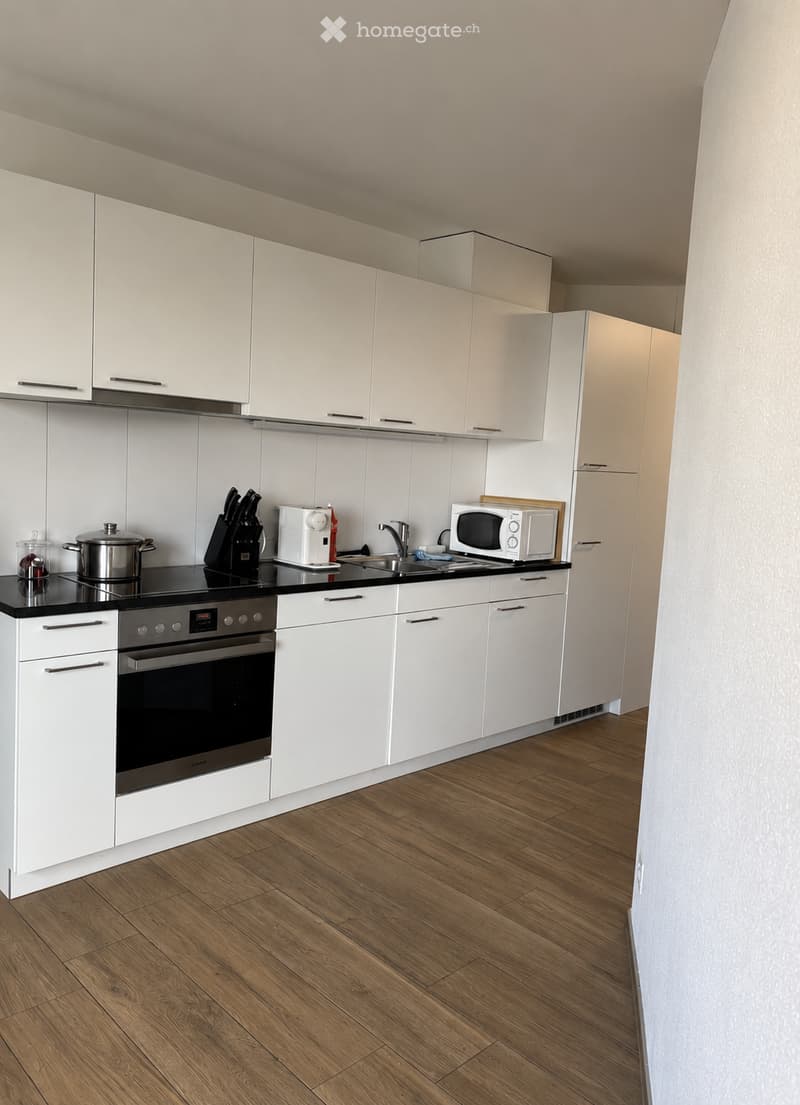 Modern kitchen with white cabinets, wooden flooring, and stainless steel appliances including an oven, microwave, and refrigerator.
