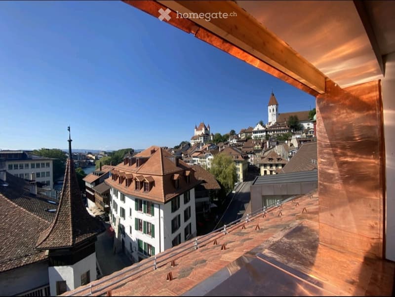 View from a balcony or terrace overlooking a historic town with traditional buildings, a church tower, and a clear blue sky.