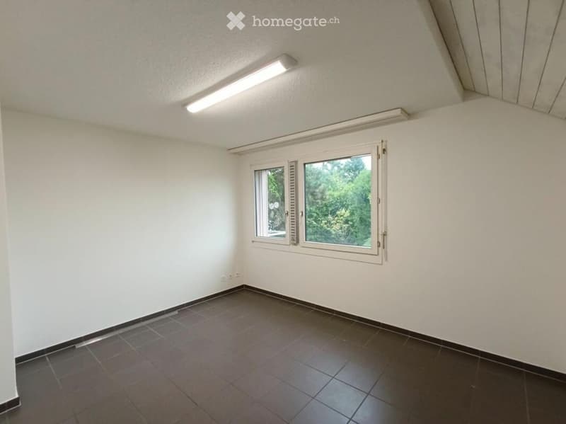 Empty room with white walls, dark tiled floor, and a large window with blinds. The ceiling has built-in lighting fixtures.