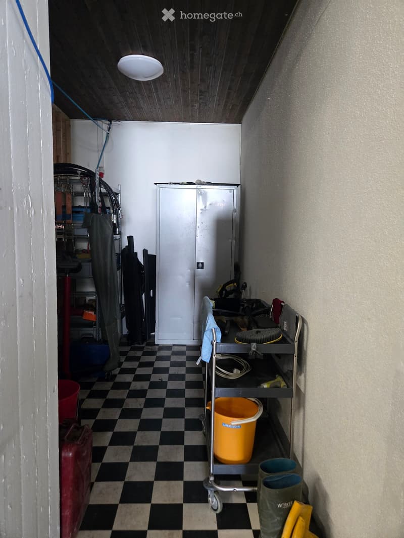 Utility room with checkered floor, refrigerator, cart with tools, buckets, boots, and gloves.