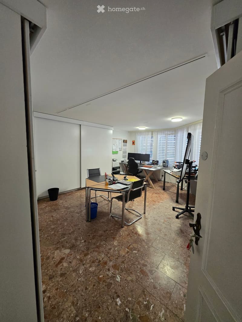 Office space with desks, chairs, computers, and a large window with blinds.