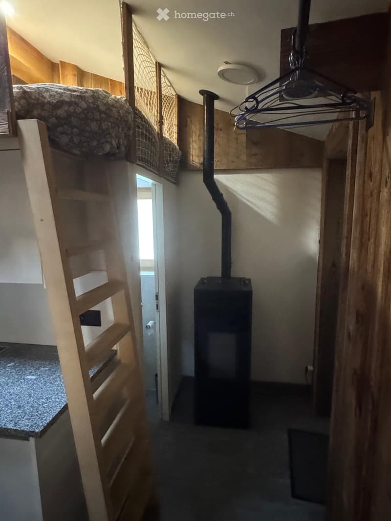 A narrow hallway with wooden walls, a staircase leading to a loft area, and a black heating unit in the center.