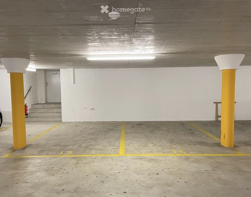 Underground parking area with marked parking spaces, yellow pillars, and a staircase leading upwards.