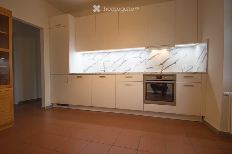 Modern kitchen with light-colored cabinets, marble backsplash, stainless steel oven, and a sink with a modern faucet.