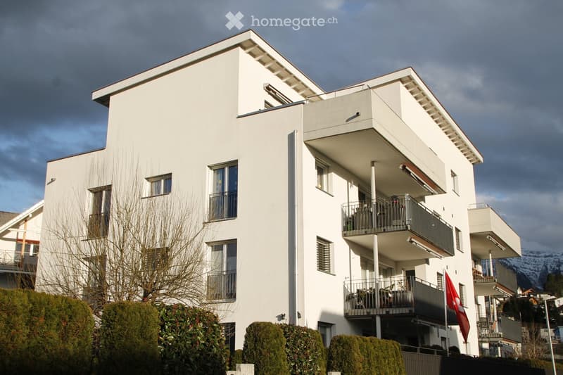 Modern white multi-story building with balconies, large windows, and a Swiss flag displayed on the facade.