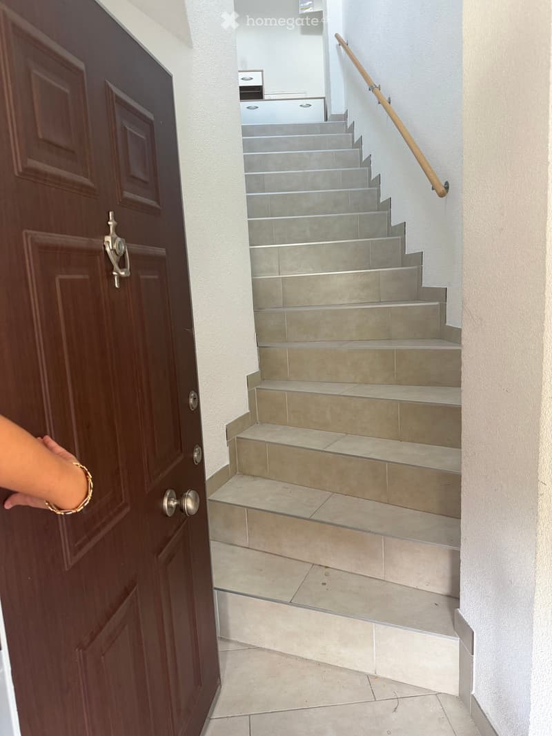 A staircase with beige tiled steps and a wooden handrail, adjacent to a dark wooden door with silver handles.