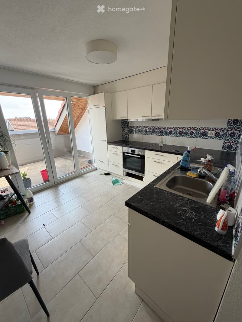Modern kitchen with white cabinets, black countertop, sink, oven, and a sliding glass door leading to a balcony.
