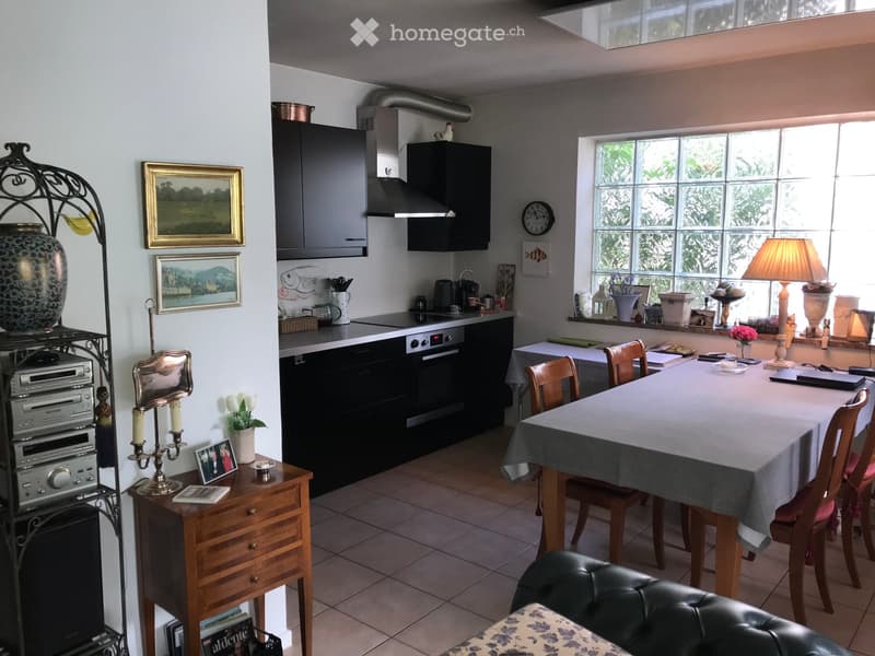 A well-lit kitchen and dining area with modern appliances, a dining table with chairs, a wooden sideboard, and decorative items including lamps, vases, and framed pictures.