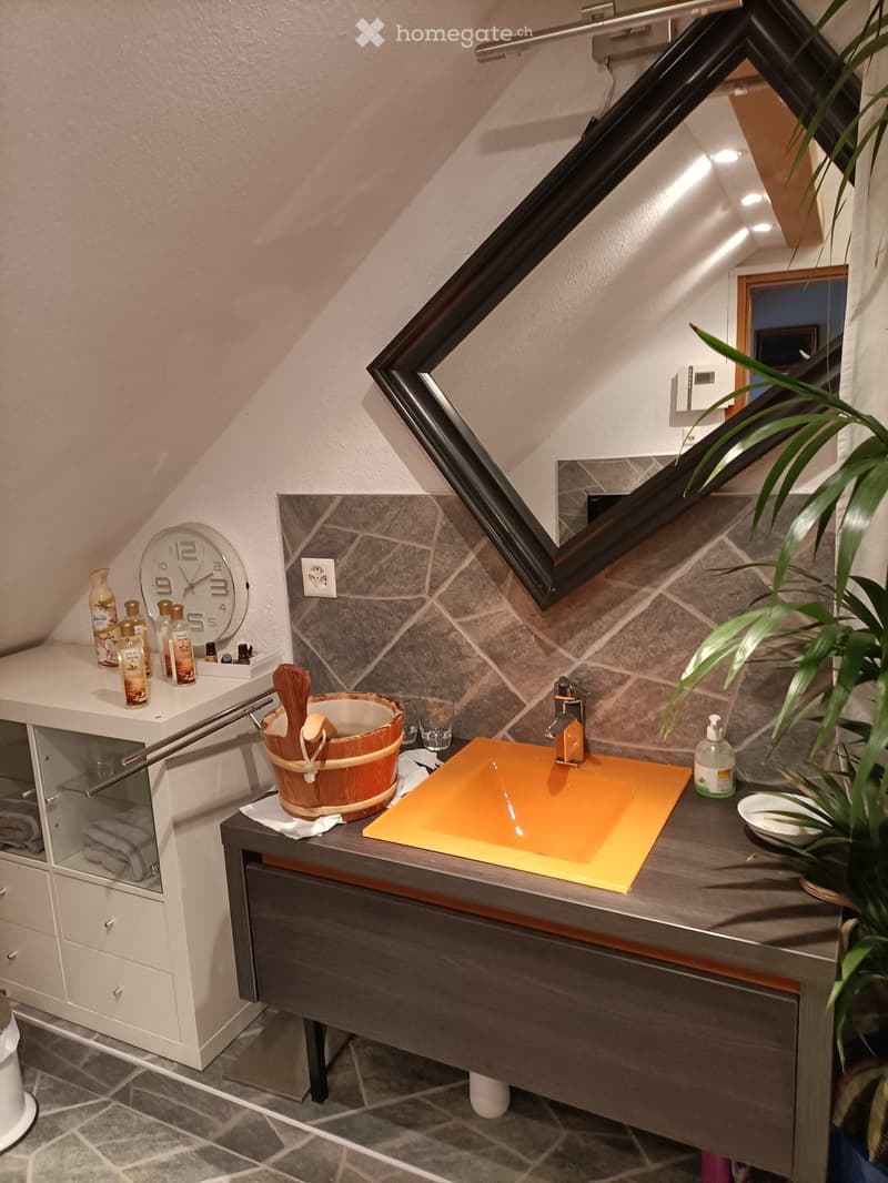 Modern bathroom with a slanted ceiling, large window, stone walls, and a wooden bucket on the counter.