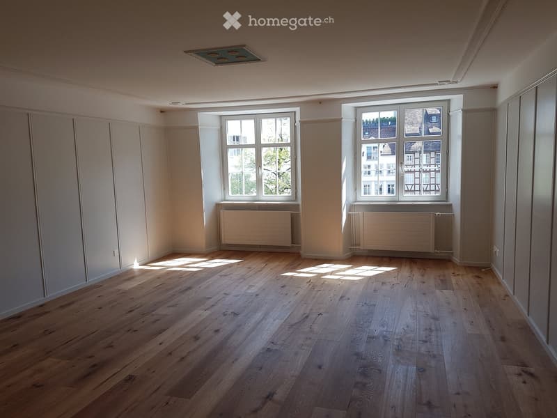 Empty room with wooden flooring, white walls, large windows, and radiators beneath the windows.