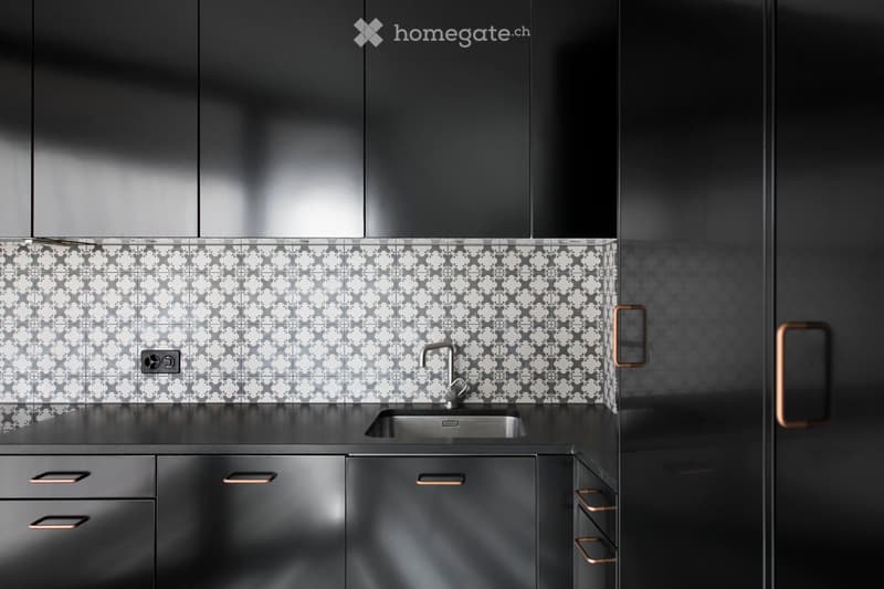 Modern kitchen with dark grey cabinets, a stainless steel sink, and patterned tiles on the backsplash.