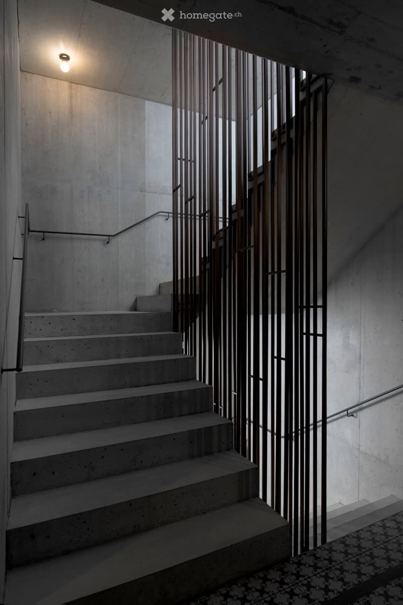 Concrete staircase with metal railings and patterned tile floor, illuminated by a single overhead light fixture.