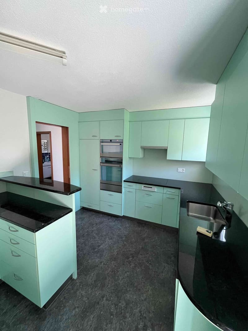 Modern kitchen with mint green cabinets, black countertops, and stainless steel appliances including an oven and sink.