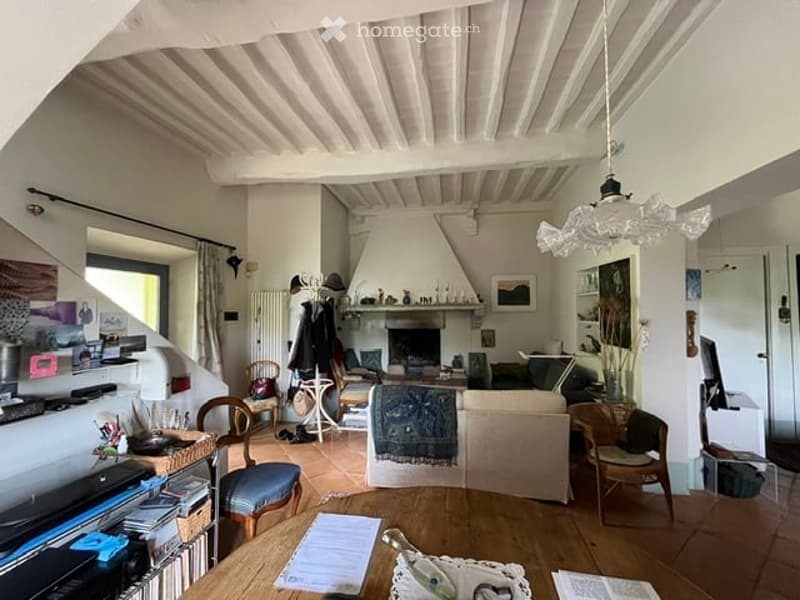 Living room with exposed wooden beams, fireplace, sofa, coffee table, chairs, and a large window with a view.