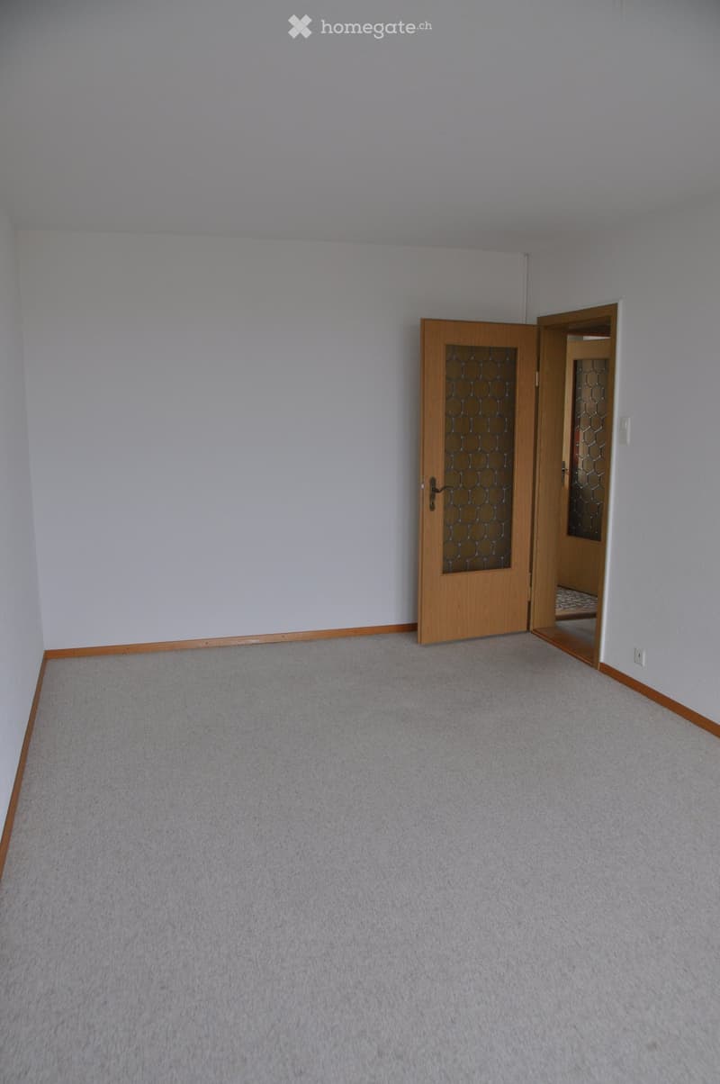 Empty room with light grey carpet and white walls, featuring a wooden door with glass panels leading to another room.