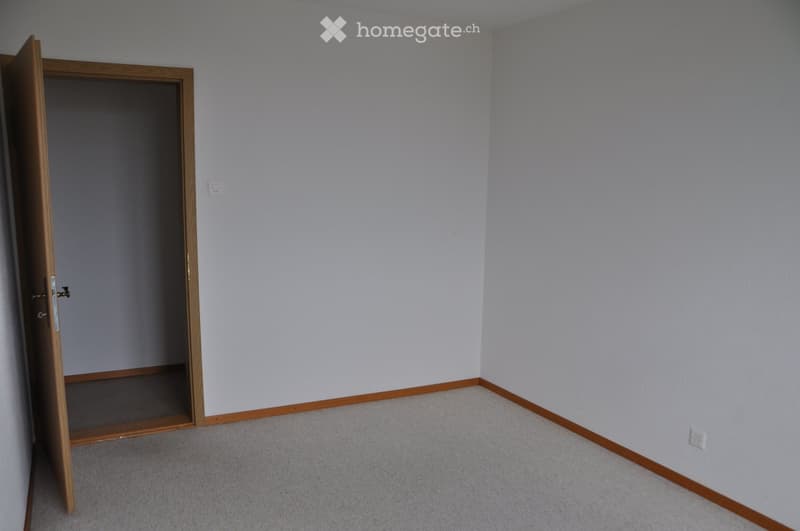 Empty room with light grey walls, carpeted floor, and a wooden door frame leading to another space.