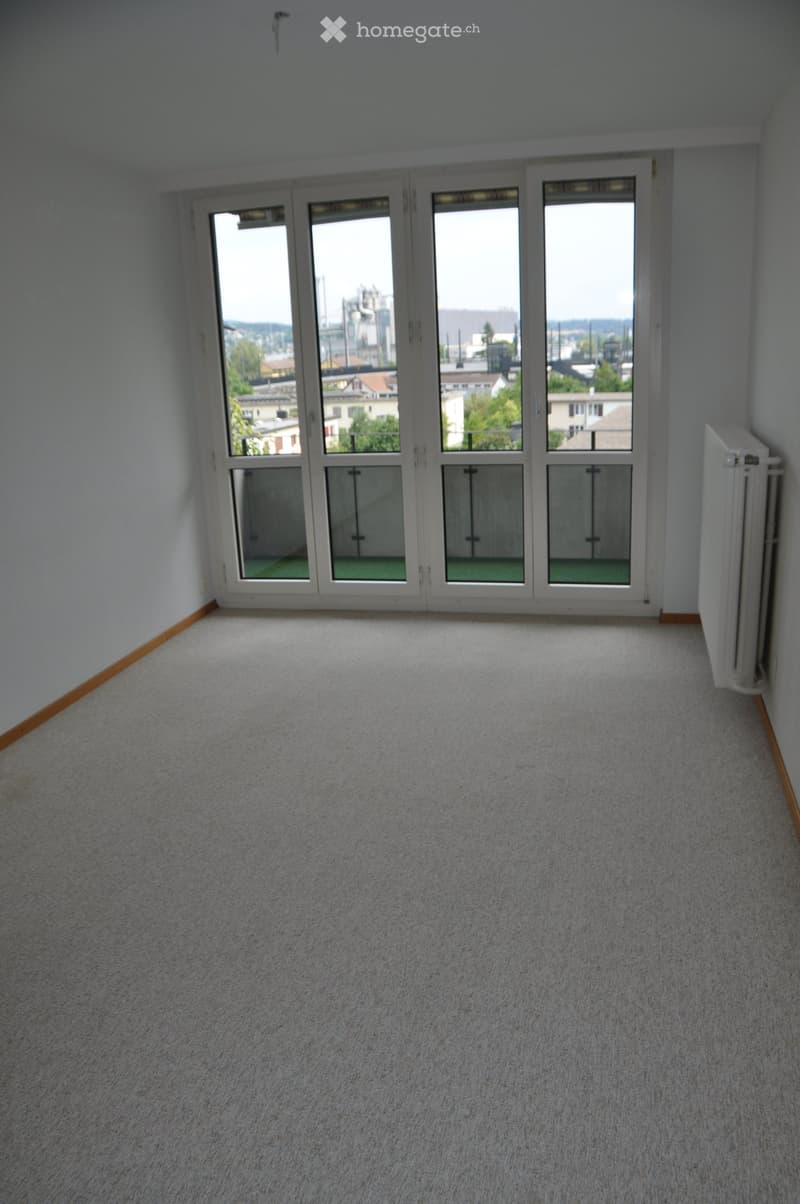 Empty room with light grey carpet, large sliding glass doors leading to a balcony, and a radiator on the right wall.