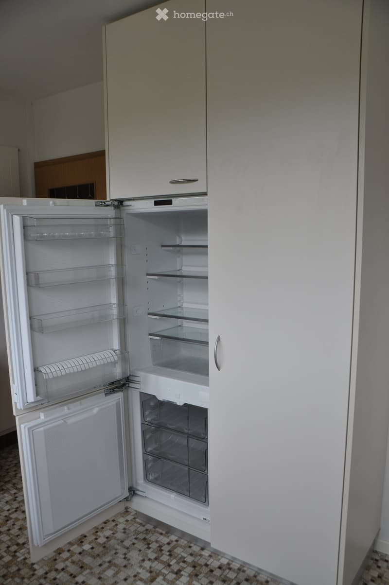 A modern kitchen with a white refrigerator featuring multiple compartments and shelves, integrated into white cabinetry.