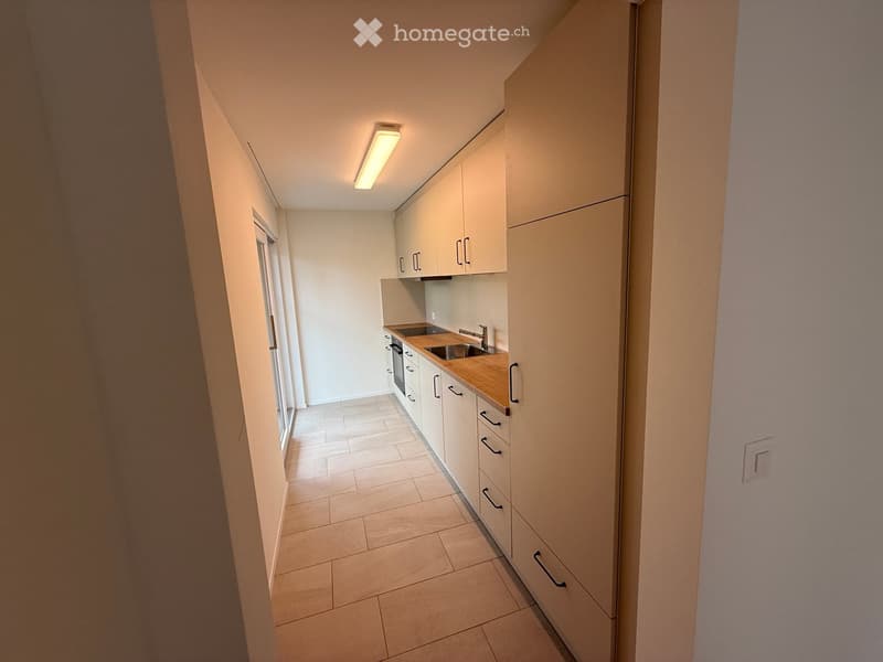 Modern kitchen with white cabinets, wooden countertop, sink, and oven. Light-colored tiled floor and walls.