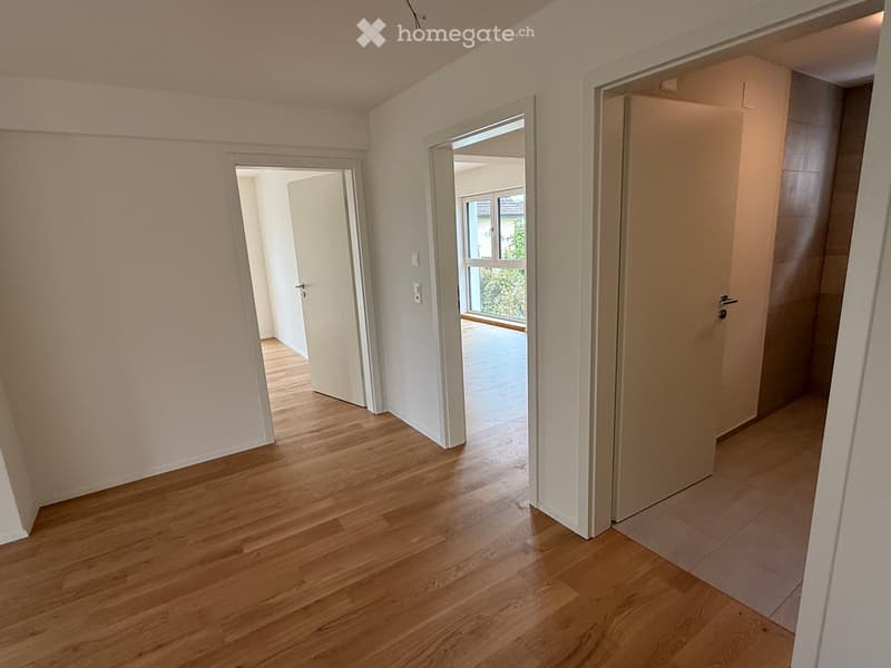Empty hallway with wooden flooring, white walls, and two open doors leading to other rooms.