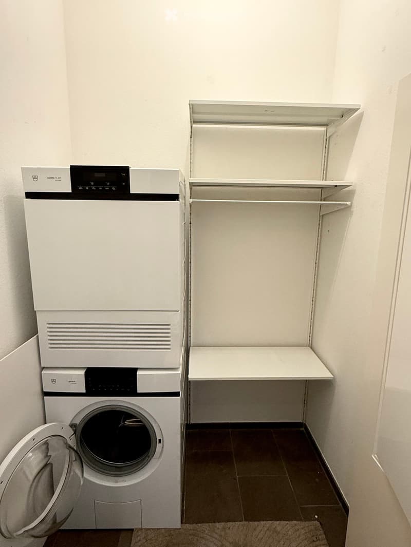 A small utility room with a white washing machine and a white dishwasher stacked vertically, with built-in shelving units on the right side.