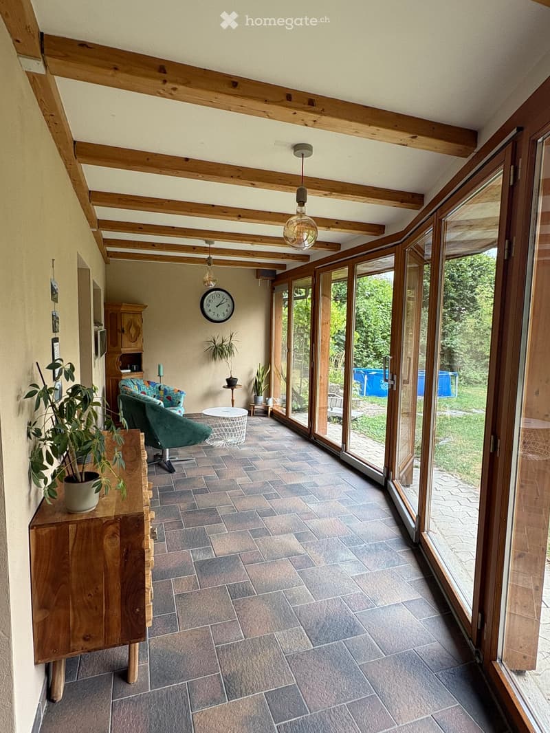 Bright, spacious room with wooden beams, large windows, tiled floor, and comfortable seating area.