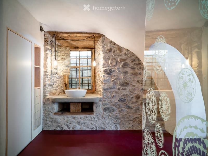 Bathroom with stone walls, a sink, and a window. The floor is red, and there is a glass partition with decorative patterns.