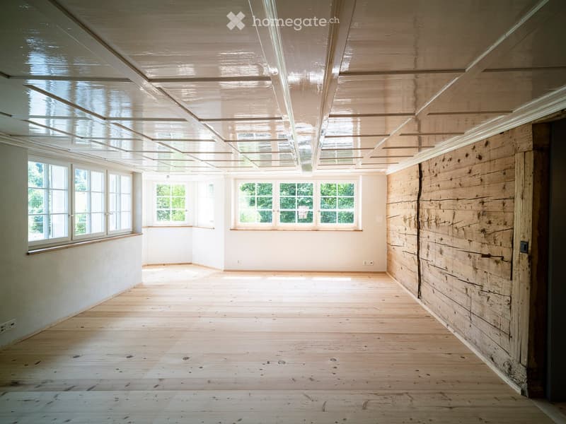 Empty room with wooden flooring, white walls, large windows, and a skylight ceiling.